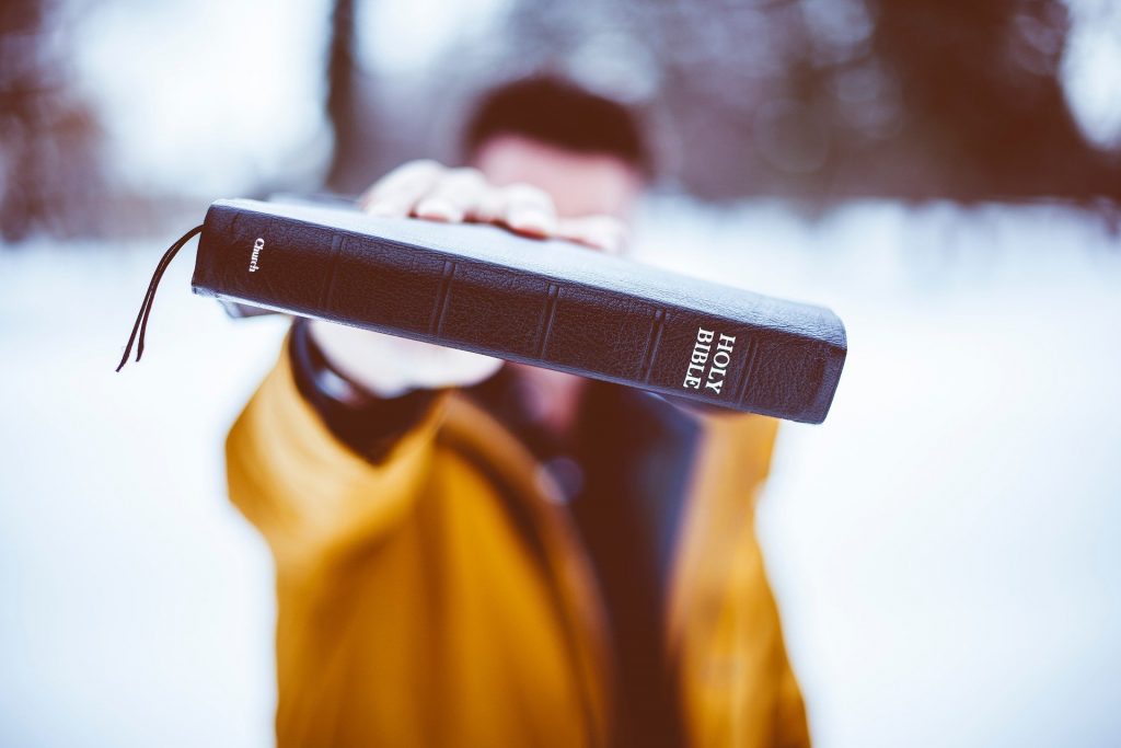 Man holding Bible in front of face.